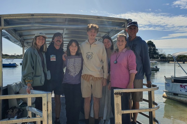 Group of people standing on a boat docked by the water on a sunny day.