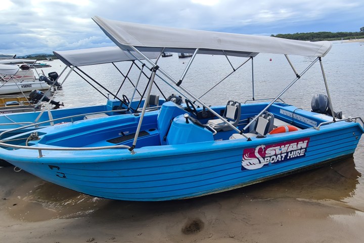 Blue boat with a canopy anchored on a sandy shore.