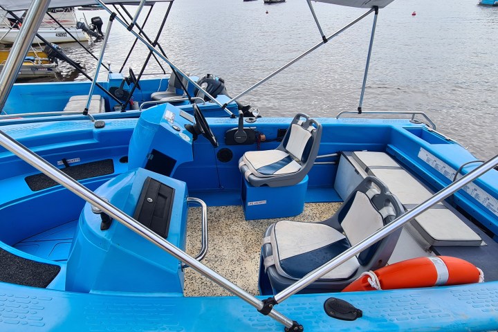 Blue motorboat with seating and console, docked on calm water.