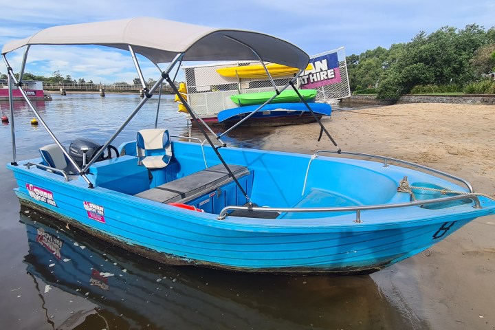 Blue motorboat with canopy on a sandy beach near a river.