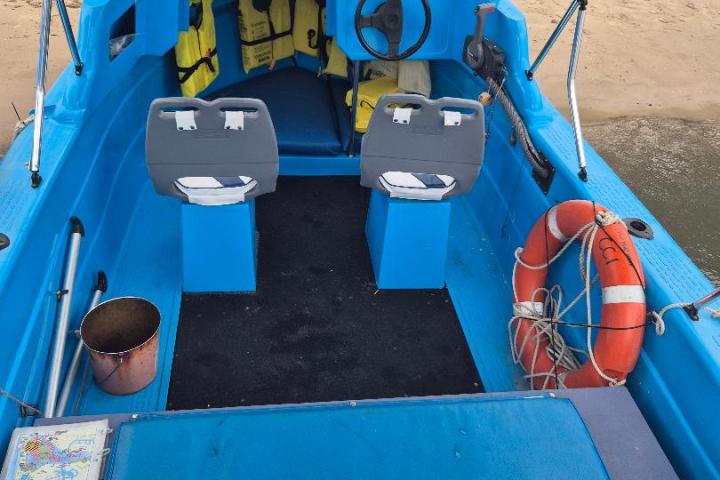 Blue motorboat with life jackets, steering wheel, and lifebuoy on sandy shore.