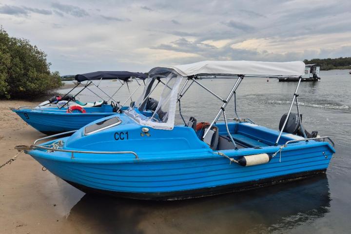 Two small blue boats with canopy roofs docked on a sandy shore by the water.