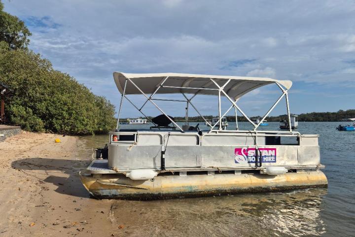 Pontoon boat beached on sandy shore with trees and water in the background.
