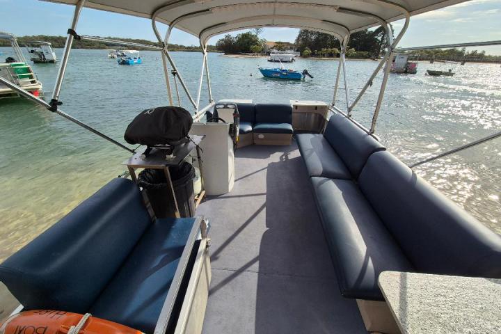 Open motorboat with blue seating under a canopy on a calm lake near other boats.