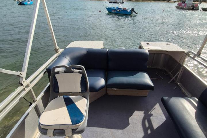 View from a boat interior with seating, steering, and a scenic lake with trees and other boats.