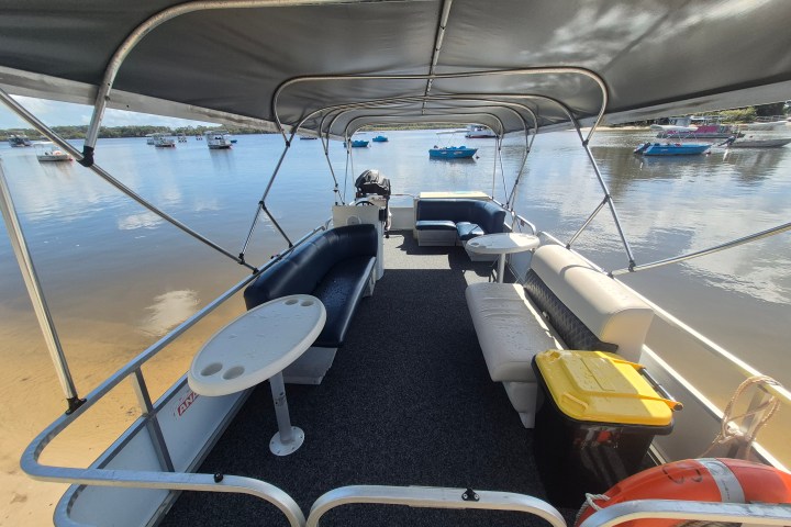 View from inside a covered pontoon boat docked by a calm lake with several boats in the background.