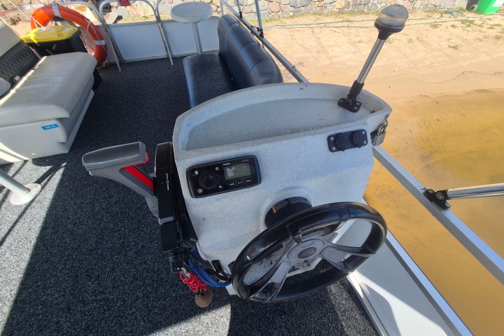 Boat helm with steering wheel and controls on carpeted deck.