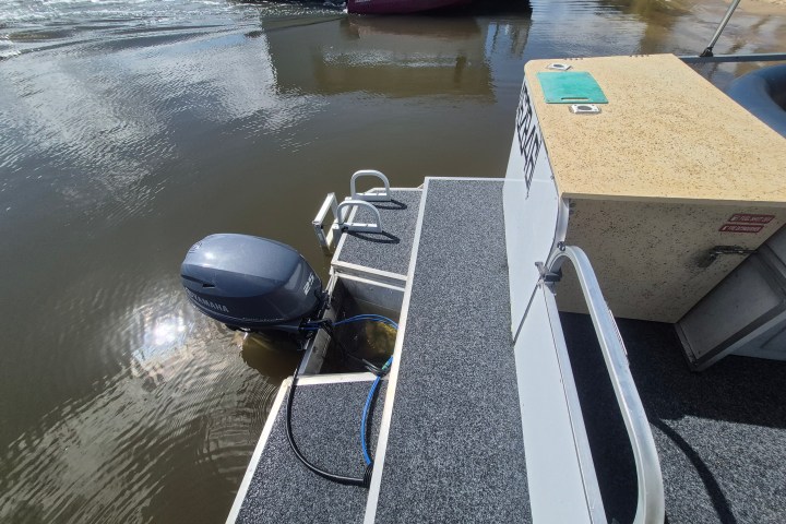 Rear deck of a boat with an outboard motor by the water.