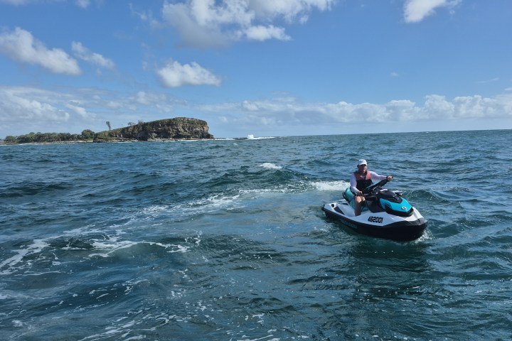 Person riding a jet ski on open water with an island in the background.