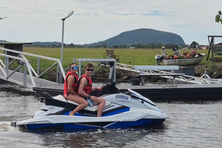 Two people on a jet ski wearing life jackets near a pier.