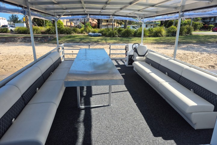 Covered boat with long table and benches, docked on a sandy beach.
