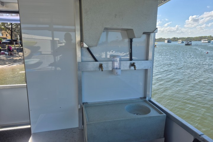Outdoor handwashing station on a boat with sink and tap, view of water and shoreline in the background.
