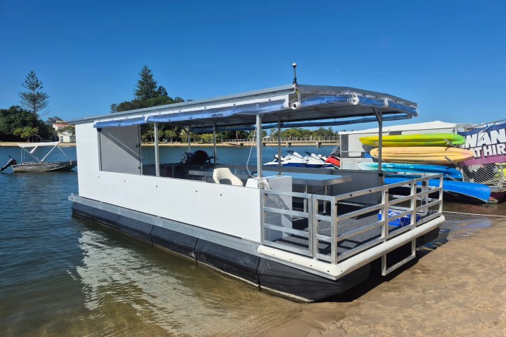A small pontoon boat docked on a sandy shore with a blue sky background.