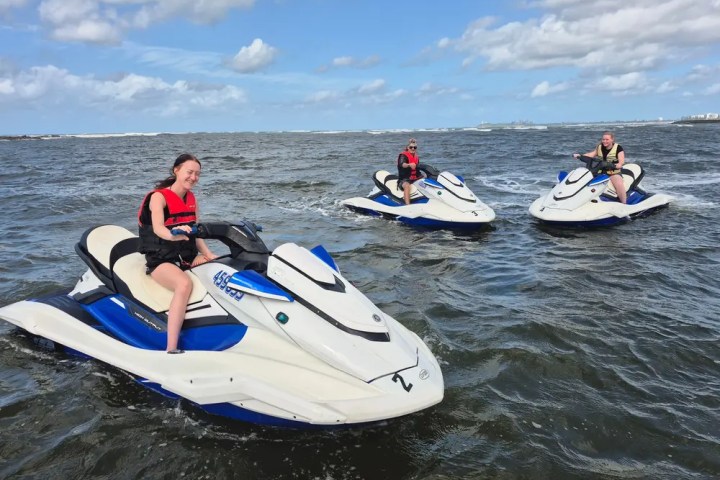 Three people on jet skis riding on open water under a cloudy sky.